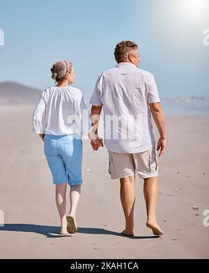 Spiaggia, estate e coppie anziane a piedi per l'esercizio mentre in vacanza, avventura o viaggio. Amate, tenendo le mani e anziani pensionati e donne Foto Stock