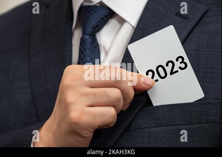 Uomo d'affari che tiene in mano un biglietto bianco con 2023 scritto su di esso. Concetto di obiettivo di business per il nuovo anno. Foto Stock