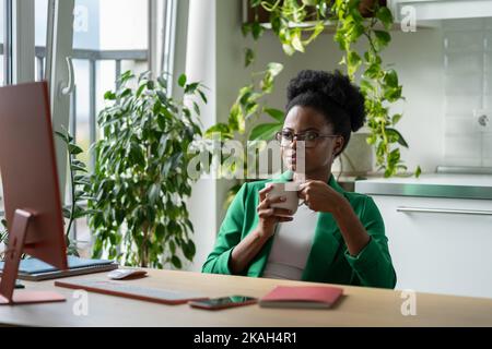 L'operaio professionale dell'ufficio della donna afroamericana che fa la rottura del caffè si siede dalla finestra al posto di lavoro Foto Stock