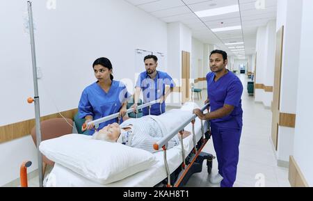 Lavoro del team medico di emergenza. Squadra concentrata di cura dell'ospedale che ruota frettolosamente la donna anziana sul gurney al reparto di emergenza dell'ospedale Foto Stock