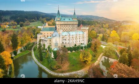 Bojnice castello. Vista aerea panoramica di un romantico castello neogotico fiabesco in un colorato giardino autunnale. Fortificazione, torri e fossato d'acqua. U Foto Stock