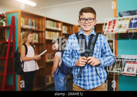 I miei libri sono imballati e pronti per andare. Ritratto di un giovane ragazzo allegro che indossa una borsa mentre si trova all'interno della biblioteca durante il giorno. Foto Stock