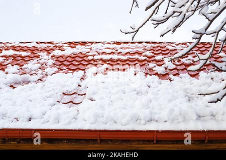 la neve scivola giù da un tetto di metallo-tegole dopo una nevicata pesante in inverno. Pericolo di caduta di neve dai tetti. Foto Stock