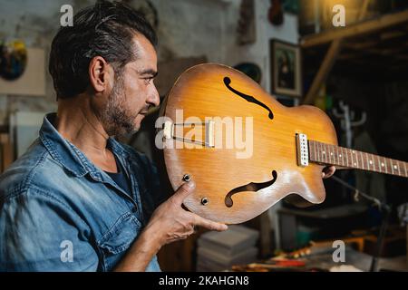 Un luzioso controlla il collo di una chitarra a corpo cavo nel suo laboratorio per verificare l'allineamento - persone, arti e concetto artigianale Foto Stock