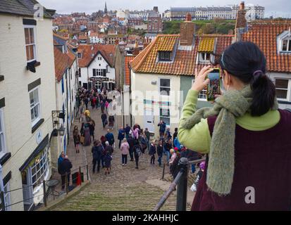 Una ragazza cinese che indossa una maschera scatta una foto sul suo telefono a Whitby Foto Stock