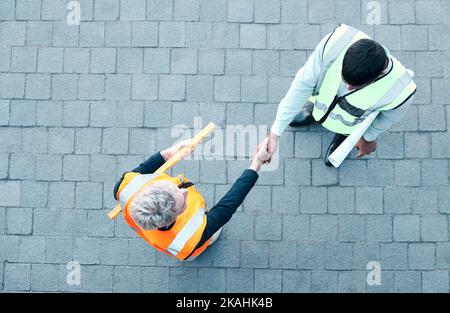 Costruzione, operai edili e artefici con vista aerea del lavoro di squadra, della collaborazione e dei project worker industriali. Gli uomini scuotono Foto Stock