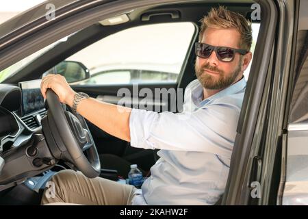 Bel giovane biondo in una camicia blu alla guida di un'auto. Foto Stock