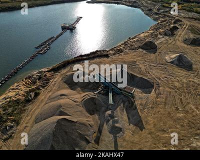 Vista aerea della miniera di minerali e delle attrezzature di estrazione presso un lago calmo nel tardo pomeriggio, evidenziando le attività industriali e i paesaggi. Foto Stock