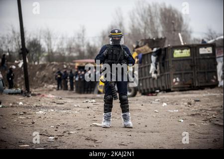 Ufficiale di polizia guardare in piedi guardia come il campo migrante 'giungla' è sgomberato il 01 marzo 2016 a Calais, Francia. Le autorità tornano a liberare i rifugi migranti da più parti del campo di migranti 'giungla' a Calais e cercano di spostare le persone verso contenitori di spedizione su un'altra parte del sito. Ieri le squadre di demolizione francesi hanno iniziato a smantellare le capanne. Si prevede che la resistenza continui e che la polizia antisommossa abbia sparato gas lacrimogeno contro i migranti che stavano gettando pietre. Una sentenza della Corte di Giovedi ha approvato un piano Govt francese per liberare parte del sito. Le autorità dicono che circa 1.000 migranti saranno colpiti Foto Stock