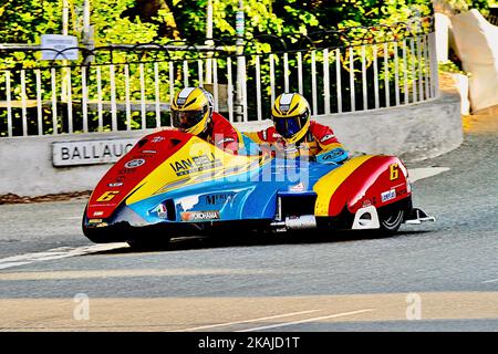 Una side car blu, gialla e rossa con due piloti durante le gare annuali del Tourist Trophy sull'Isola di Man, Regno Unito Foto Stock