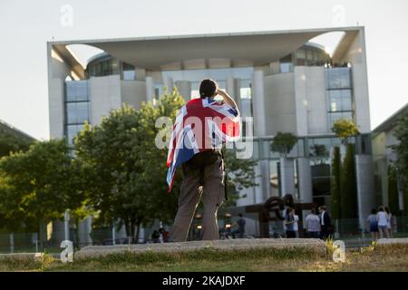 Un uomo che indossa la bandiera britannica Union Jack guarda alla Cancelleria mentre la cancelliera tedesca Angela Merkel e il primo ministro britannico Theresa May si incontrano a Berlino, in Germania, il 20 luglio 2016. Foto Stock