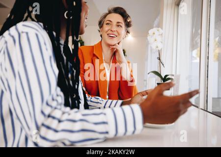 Donne d'affari sorridenti che hanno una discussione mentre si siedono insieme in una caffetteria. Due colleghi di lavoro donne felici che condividono idee durante un caffè Foto Stock