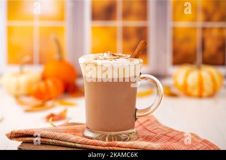 Latte speziato di zucca a base di piante con panna montata senza latticini a base di cocco ricoperta di cannella in una scena festiva cucina autunnale Foto Stock