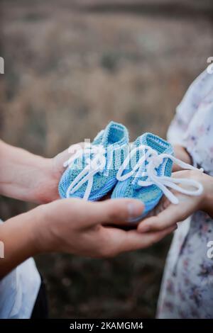 father and mother hold newborn's shoes close-up Foto Stock