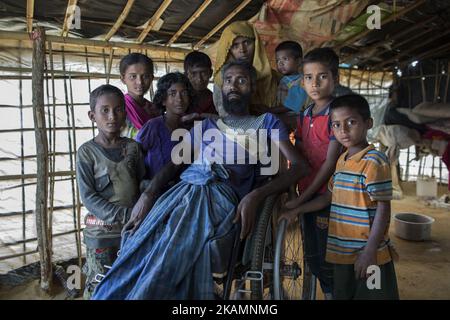 Un ritratto di Mohammad Alamgir, 40 anni, e della sua famiglia. Mohammad è disabile a causa della poliomielite, è fuggito con la sua famiglia dalle recenti violenze in Myanmar e si è rifugiato nel campo profughi di Kutupalong, il bazar di Cox. Circa 70.000 musulmani Rohingya sono fuggiti dal Myanmar al Bangladesh dal 9 ottobre 2016 dopo che i militari birmani hanno lanciato operazioni di sdoganamento. L'ufficio per i diritti umani delle Nazioni Unite ha dichiarato nel loro rapporto che le forze di sicurezza del Myanmar hanno commesso uccisioni di massa, torture e stupri di bande di Rohingyas, così come hanno bruciato i loro villaggi. Rohingyas cominciò a fuggire dall'oppressione militare, la prima nel 1978 Foto Stock