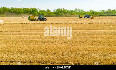 Vista dall'alto del trattore come rotopressa, macchina che arrotola la paglia e spola una balla rotonda imballata sul campo agricolo. Foto Stock