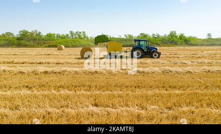 Vista dall'alto del trattore come rotopressa, macchina che arrotola la paglia e spola una balla rotonda imballata sul campo agricolo. Foto Stock