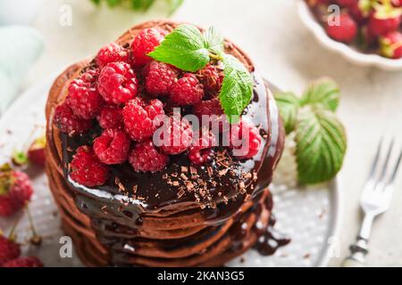 Pancake al cioccolato. Frittelle con lampone fresco con glassa al cioccolato o condimenti in recipiente grigio su sfondo grigio chiaro tavolo. Ameri classici fatti in casa Foto Stock