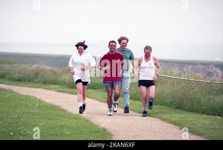 1998, primavera e quattro persone che corrono insieme fuori sul sentiero costiero, partecipando a una corsa di beneficenza, tre in pantaloncini corti, uno con jeans demini, South Shields, Tyne and Wear, Inghilterra, Regno Unito. Foto Stock