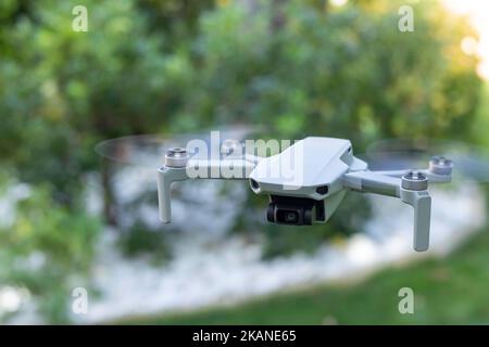 Vista ravvicinata del piccolo drone che vola controllato da un essere umano dal telecomando in uno sfondo verde Foto Stock