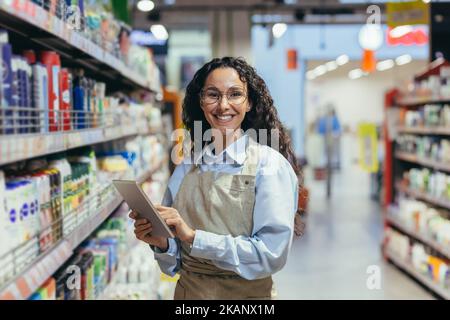 Ritratto di felice e di successo venditore donna, ispanica con capelli ricci sorridendo e guardando la fotocamera, utilizzando il tablet computer per rivedere il prodotto. Foto Stock