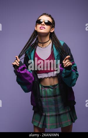 Giovane donna in vintage abiti e occhiali da sole in piedi isolato su viola, immagine stock Foto Stock