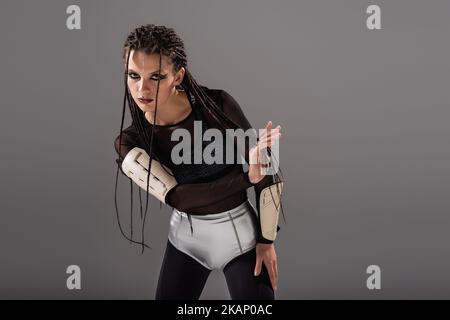 donna futuristica con dreadlock in posa in tuta stretta e pantaloncini in argento isolato su grigio, immagine stock Foto Stock