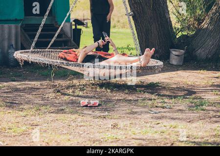 Donna con smartphone in amaca rotonda all'ombra dell'albero Foto Stock