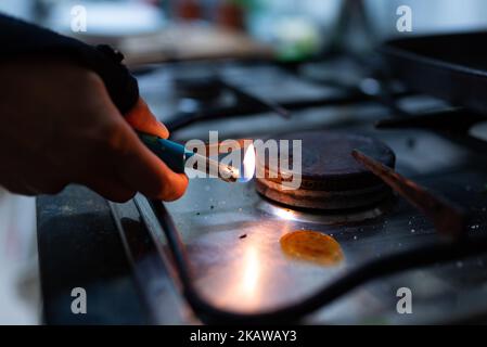 Si vede una mano che tiene un accendino mentre accende il bruciatore a gas di una stufa da cucina. A causa dell'invasione russa dei prezzi del gas in Ucraina hanno raggiunto la recor Foto Stock