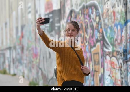 Una signora turistica prende un selfie vicino ai dipinti murali politici e sociali sulla barriera israeliana della Cisgiordania a Betlemme, in Cisgiordania, il 13 marzo 2018. (Foto di Artur Widak/NurPhoto) Foto Stock