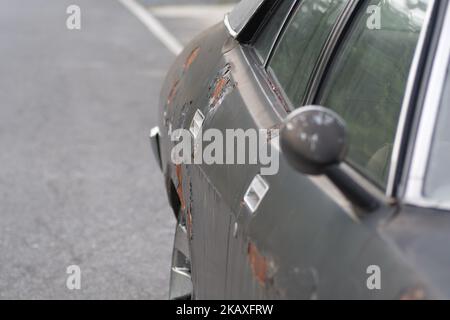 Il lato della vettura nera con le parti arrugginite intemperie parcheggiate su strada asfaltata Foto Stock