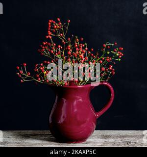 Mazzetto di bacche rosse sul tavolo in un vaso rosso. Foto Stock