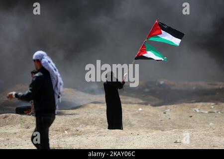 Una donna detiene una bandiera palestinese durante gli scontri con le forze israeliane vicino al confine tra la striscia di Gaza e Israele, a est di Gaza City il 14 maggio 2018, a seguito della controversa mossa a Gerusalemme dell'ambasciata degli Stati Uniti. (Foto di Momen Faiz/NurPhoto) Foto Stock