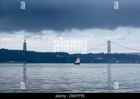 Un'antica barca passa dal Ponte 25 de Abril e dal Santuário de Cristo Rei sulla passeggiata Tejo lungo il fiume Tago (Rio Tejo), Lisbona, Portogallo, Marc Foto Stock