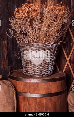 Fiori secchi in un cesto di vimini su un barile di legno. Stile retrò Foto Stock