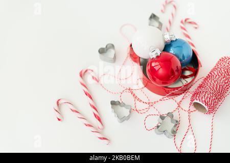 Le caramelle di Natale, insieme ai taglierini dei biscotti, ai giocattoli dell'albero di Natale ed al filo rosso per il rivestimento del regalo, si trovano su un tavolo bianco. Messa a fuoco selettiva, rumore. CHRI Foto Stock