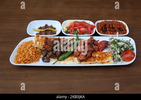 Kebab di fegato e kebab di agnello shish sono sul piatto, accompagnati da insalata, pasta piccante e polpette crude Foto Stock