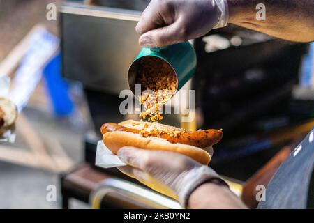Primo piano dello chef che tiene una salsiccia in un rotolo, hot dog con leoni tirati sopra, cibo di strada, pranzo, snack, Foto Stock