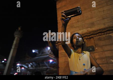 Un piccolo gitls scatta le foto mentre le ragazze e le donne nepalesi bevono la birra Santa del riso si riversa dalla bocca la maschera enorme di idolo Swet Bharab durante il festival di Indra Jatra celebrato a Basantapur Durbar Square, Kathmandu, Nepal mercoledì 26 settembre 2018. Indra Jatra è la celebrazione del giorno di Dio Indra, il re dei cieli. Indra Jatra è festival si celebra in Basantapur Durbar Square, Kathmandu, Nepal. Indra Jatra è uno dei festival importanti del Nepal che celebra la fine del monsone. Il festival più grande in cui Kumari si presenta al pubblico è Indra Jatra. Su quanto segue Foto Stock