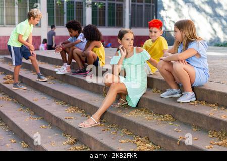 I tweenager positivi si fanno baffare mentre si siedono sui gradini all'aperto Foto Stock