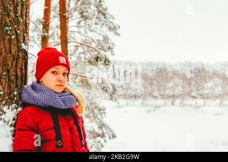 una ragazza in giacca rossa sta in piedi nella foresta ridendo in inverno sullo sfondo di una foresta innevata. Foto Stock