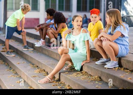 I tweenager positivi si fanno baffare mentre si siedono sui gradini all'aperto Foto Stock