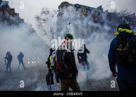 Un protester 'Gilets Jaunes' ('Yellow Vest') guarda indietro verso la polizia antisommossa francese mentre il gas lacrimogeno riempie l'aria durante una dimostrazione negli Champs Elysees Avenue a Parigi, in Francia, il 15 dicembre 2018. Nonostante i ministri del governo francese si appellino alle proteste a livello nazionale dei Gilets Jaunes (gilet giallo) per fermarsi a seguito dell'attacco di Strasburgo che ha ucciso tre persone il 11 dicembre, i manifestanti hanno preso le strade della Francia per il quinto sabato consecutivo. Il movimento 'Gilets Jaunes' ('Yellow Vest') - iniziato il 17 novembre 2018 e ispirato dall'opposizione ad una nuova tassa sui carburanti - ha assorbito Foto Stock