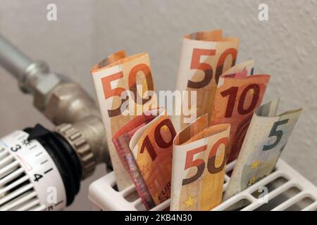 Banconote di carta euro inserite nel radiatore di riscaldamento a casa. Un simbolo dell'aumento dei costi di riscaldamento. Soldi per pagare le fatture. Foto Stock