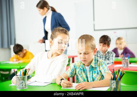 Felice di chattering alunni seduti a lezione a scuola elementare Foto Stock
