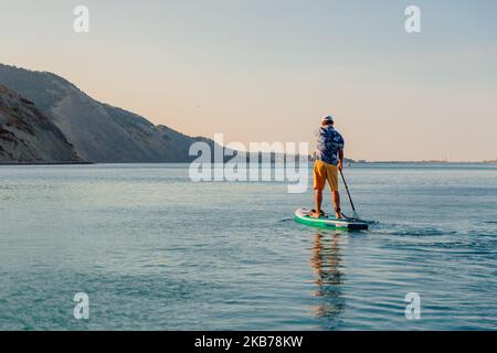 Luglio 29, 2022. Dalaman, Turchia. Uomo in camicia hawaiana a bordo di paddle SUP sul mare tranquillo. Stile di vita estivo attivo Foto Stock