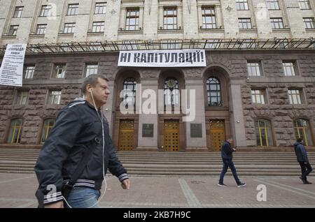 La gente passa davanti a una bandiera che legge 'No alla capitolazione!', contro l'attuazione della cosiddetta 'Steinmeier Formula', che ha installato sopra l'ingresso al municipio di Kyiv, Ucraina, il 04 ottobre 2019. Il 1 ottobre, 2019 membri del Gruppo di contatto trilaterale sull'Ucraina hanno accettato un processo di pace noto come "Steinmeier Formula", come hanno riferito i media locali. (Foto di Str/NurPhoto) Foto Stock