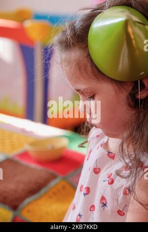 bambina in un cappello da festa che mangia la torta al primo compleanno di suo fratello Foto Stock