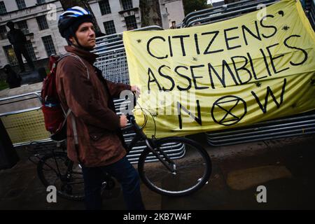 Un uomo spinge una bicicletta oltre una bandiera che chiede ai cittadini assemblee come gruppo attivista sul cambiamento climatico Extinction Rebellion (XR) bloccare le strade il giorno di apertura della sua lunga 'ribellione Internazionale' a Londra, Inghilterra, il 7 ottobre 2019. I membri del gruppo intendono occupare 12 siti intorno agli edifici governativi di Westminster almeno fino a sabato 19 ottobre prossimo, con l'obiettivo di "mettere in secondo piano" l'area per esercitare pressioni sui legislatori affinché intraprendano ulteriori e più rapidamente azioni per arrestare la perdita di biodiversità e ridurre le emissioni di gas a effetto serra. Blocchi simili da Extinction Rebellion nella città nel mese di aprile, nei siti in Foto Stock