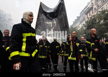 Firemen march in the procession in intervention gear, one of them wearing his hood, in front of a large banner representing a dead fireman accompanied by the character of the mower, representing death, on Tuesday, October 15, 2019, while several thousand professional firemen demonstrated in the streets of Paris for a major day of national mobilization at the call of all the unions. The purpose of this day of mobilization was to denounce their working conditions, their lack of resources and non-recognition as a high-risk occupation. (Photo by Samuel Boivin/NurPhoto) Stock Photo